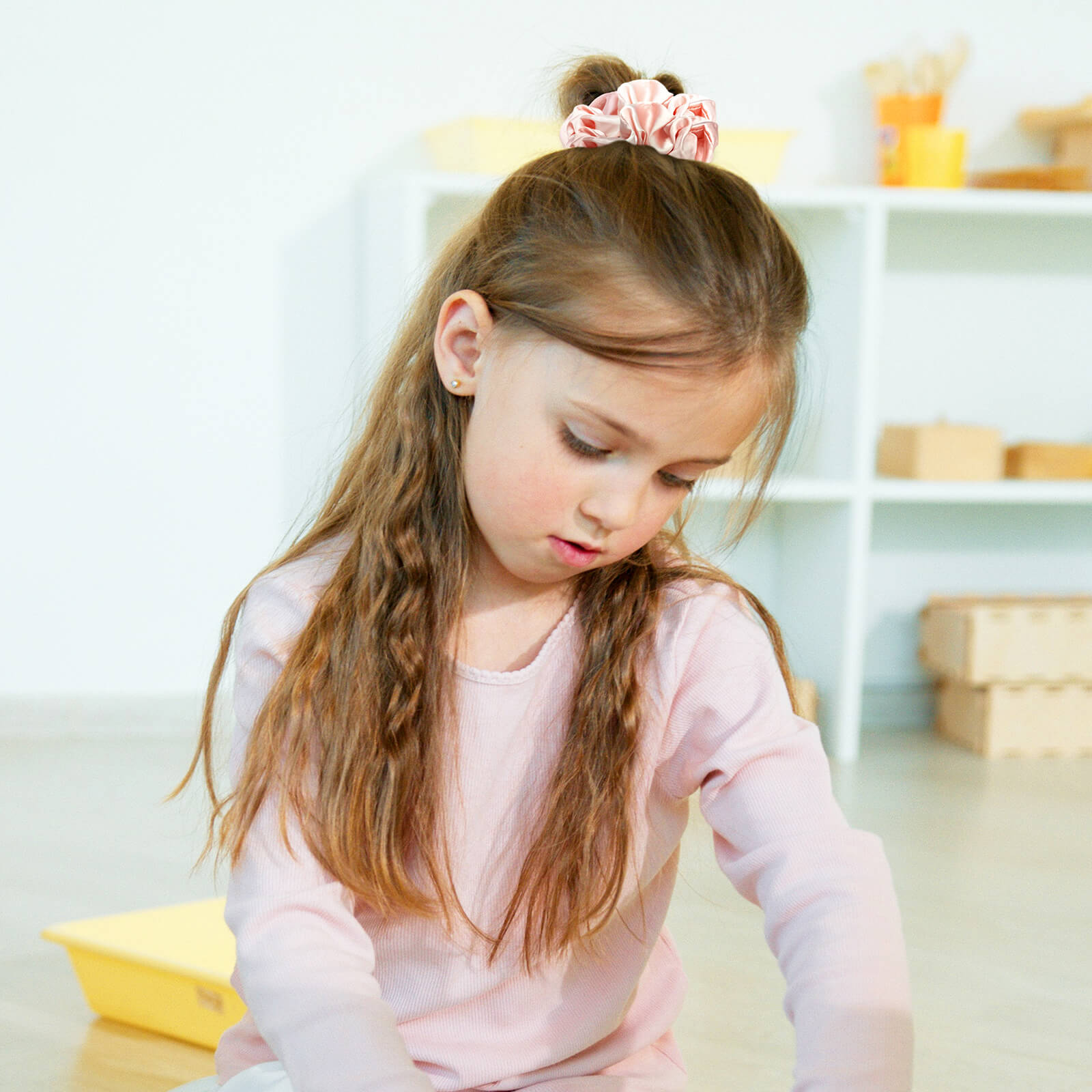 A girl with her hair in a loose bun held by a black Lolalet satin sleep scrunchy, protecting her hair overnight.