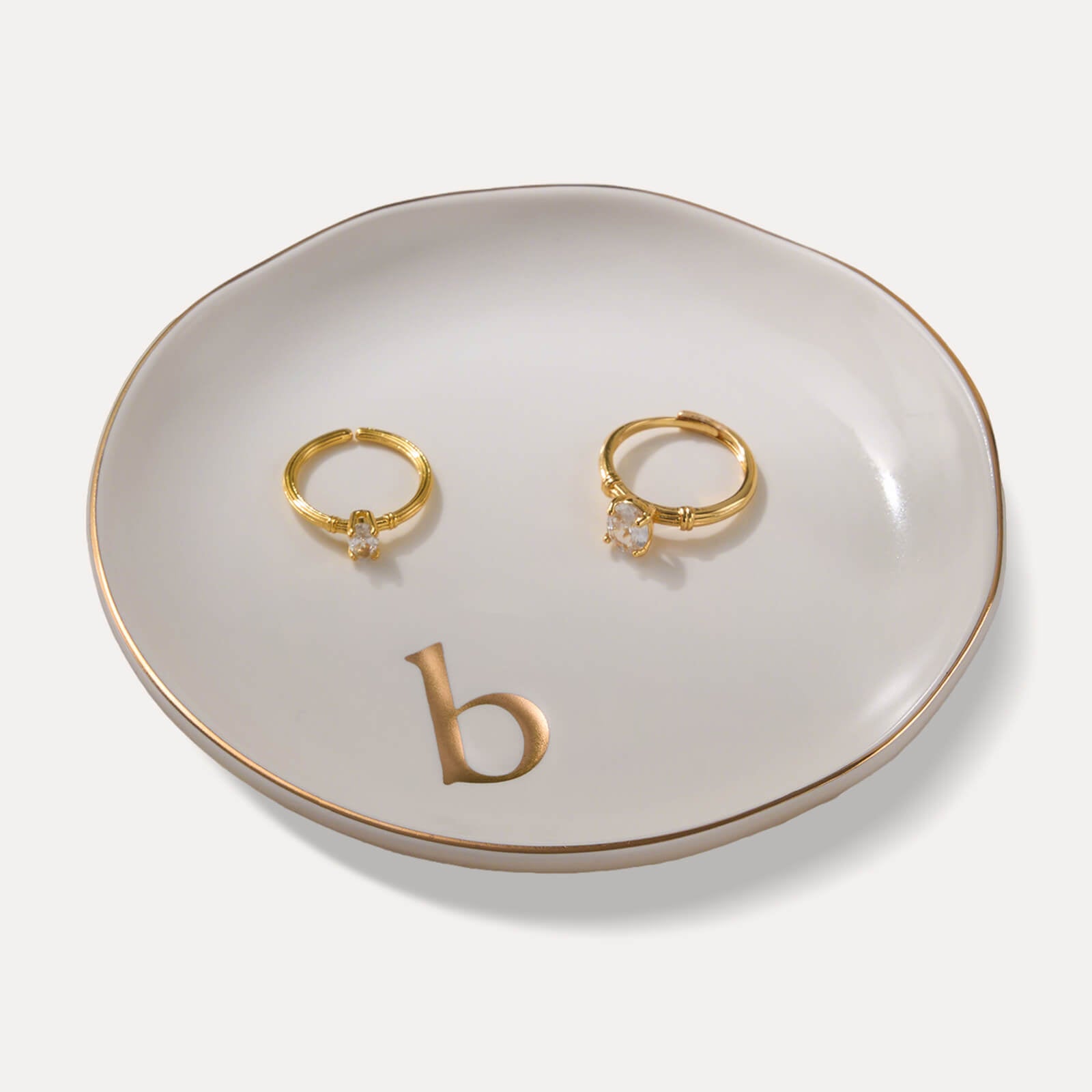 A Lolalet white ceramic jewelry dish featuring a gold "b" initial, elegantly holding an engagement ring, serving as a monogrammed ring holder.