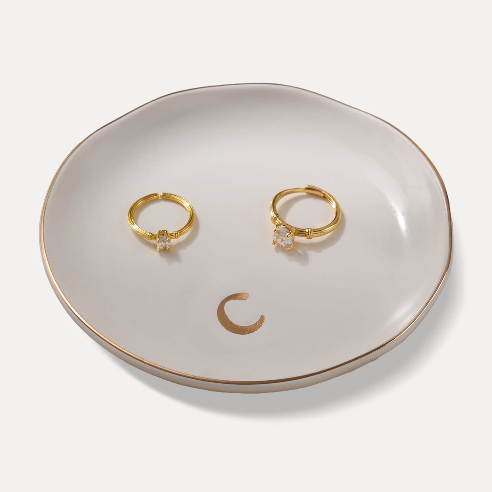 A Lolalet white ceramic jewelry dish featuring a gold "c" initial, elegantly holding an engagement ring, serving as a monogrammed ring holder.