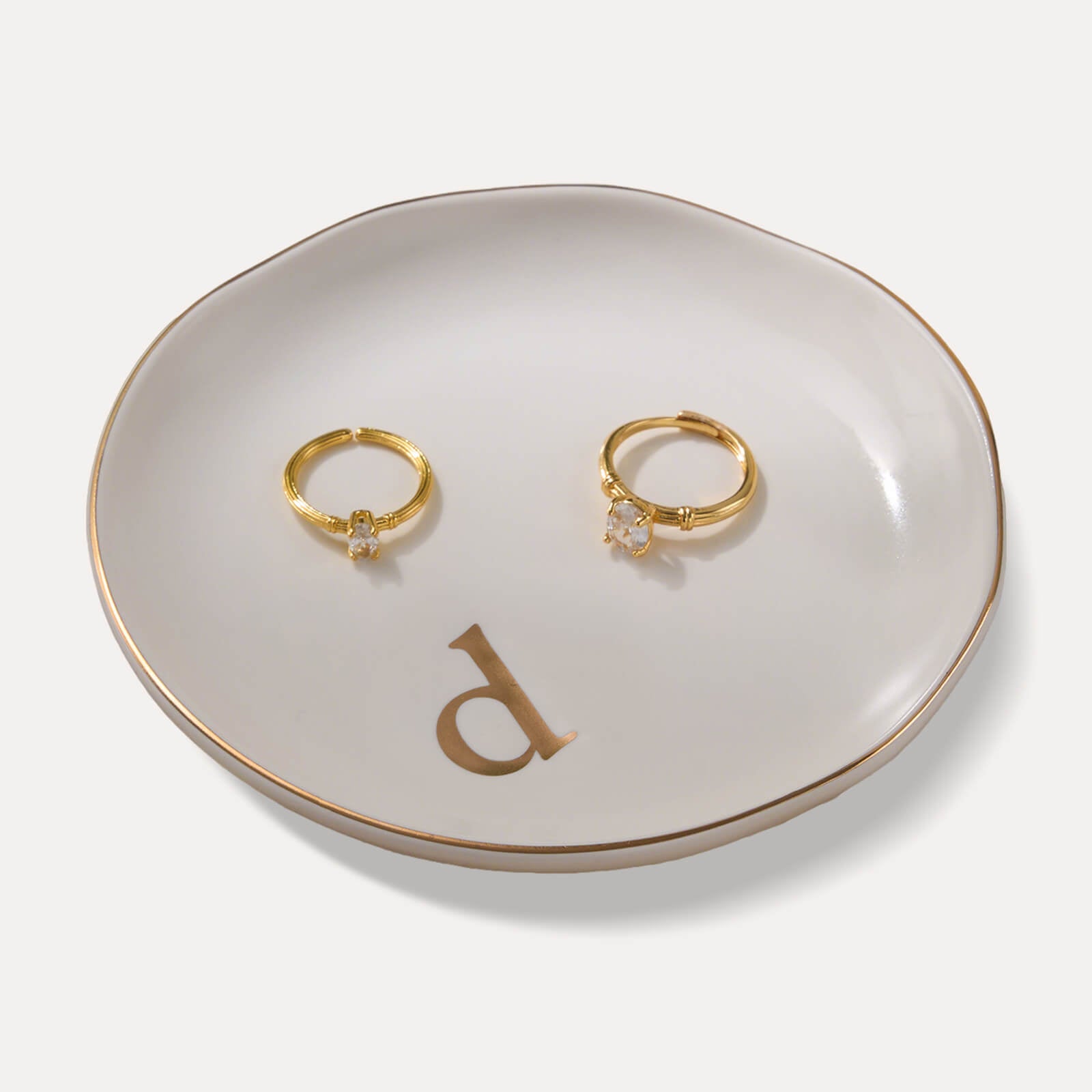 A Lolalet white ceramic jewelry dish featuring a gold "d" initial, elegantly holding an engagement ring, serving as a monogrammed ring holder.