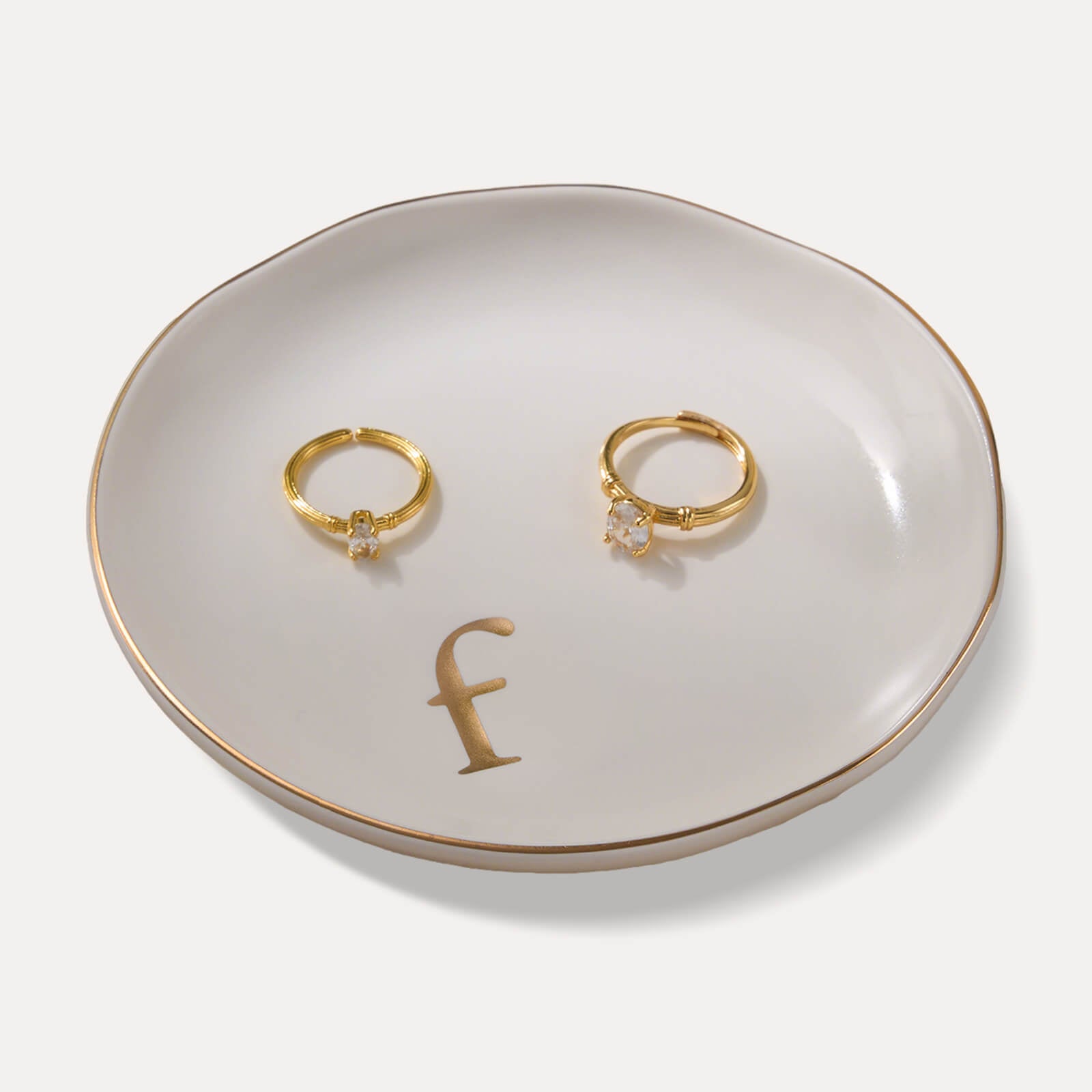 A Lolalet white ceramic jewelry dish featuring a gold "f" initial, elegantly holding an engagement ring, serving as a monogrammed ring holder.