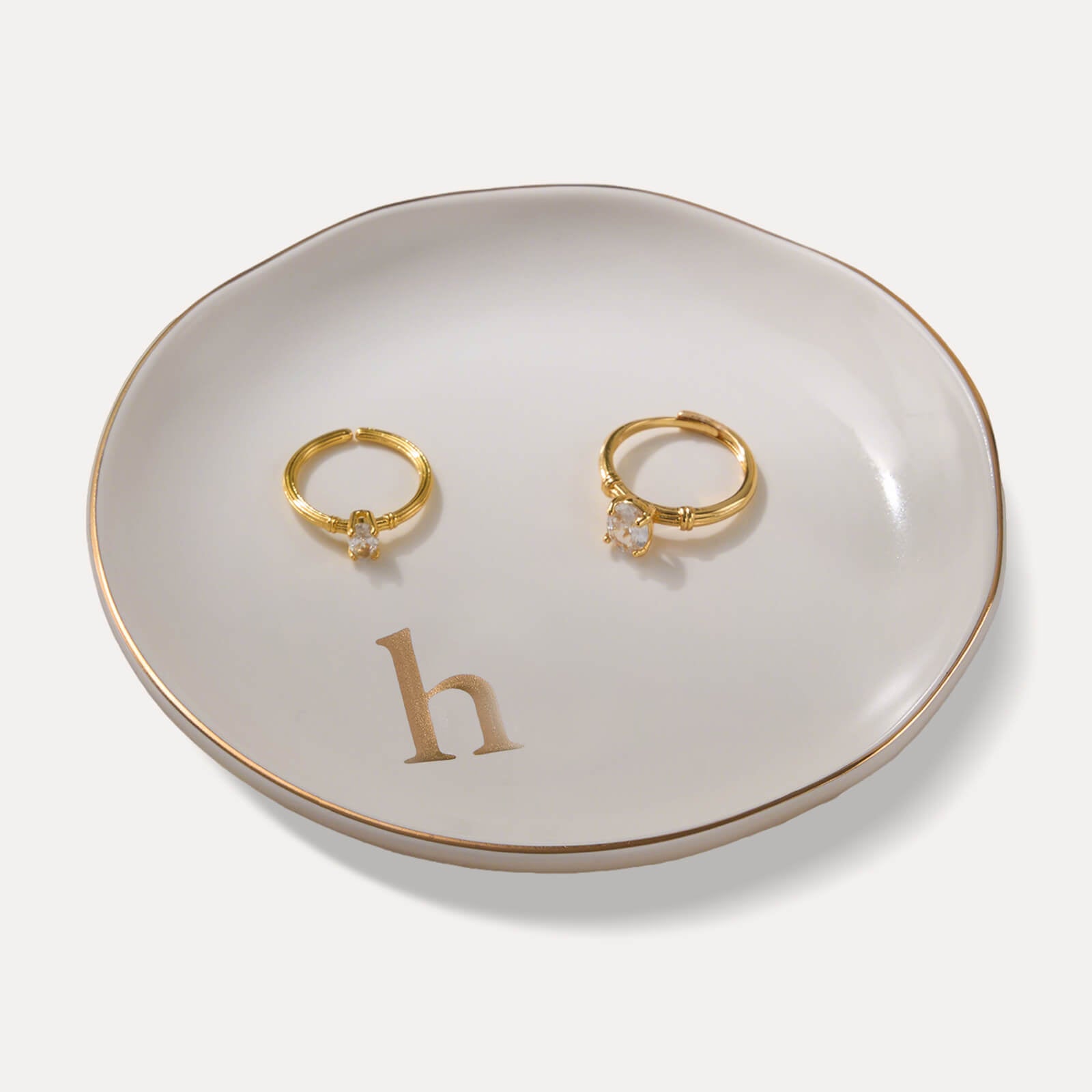 A Lolalet white ceramic jewelry dish featuring a gold "h" initial, elegantly holding an engagement ring, serving as a monogrammed ring holder.