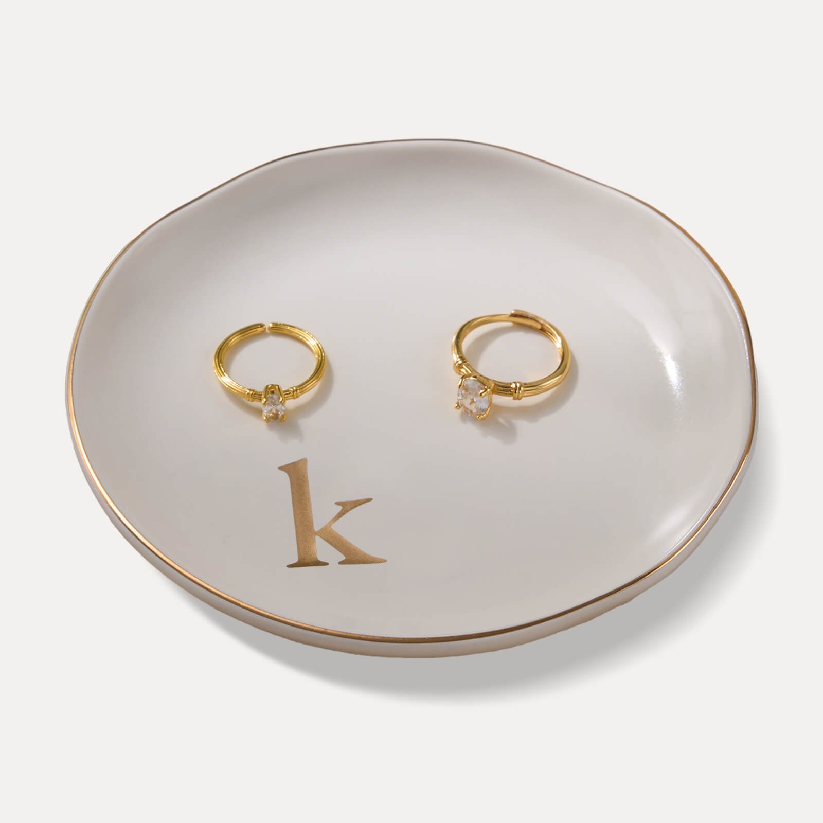 A Lolalet white ceramic jewelry dish featuring a gold "k" initial, elegantly holding an engagement ring, serving as a monogrammed ring holder.