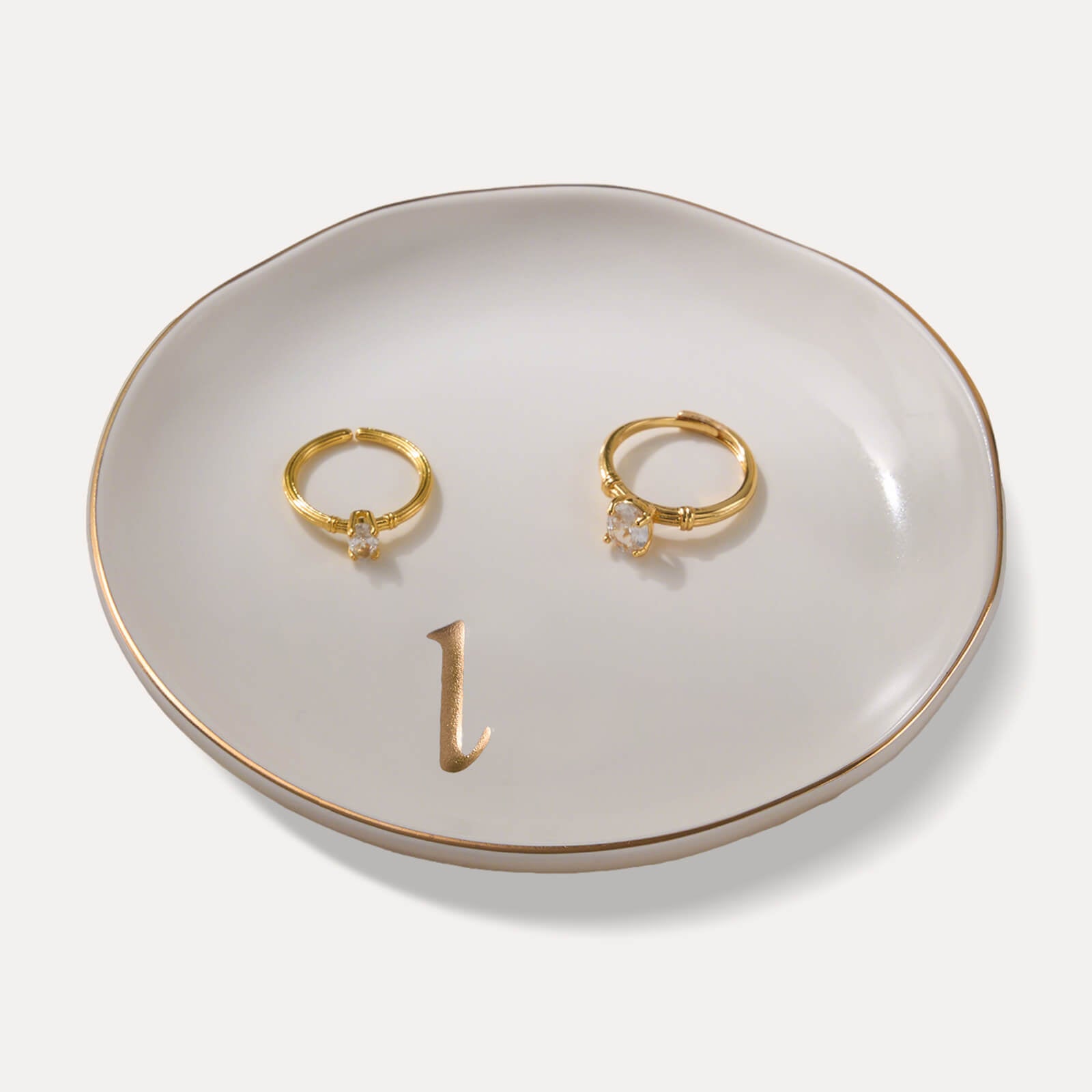 A Lolalet white ceramic jewelry dish featuring a gold "l" initial, elegantly holding an engagement ring, serving as a monogrammed ring holder.
