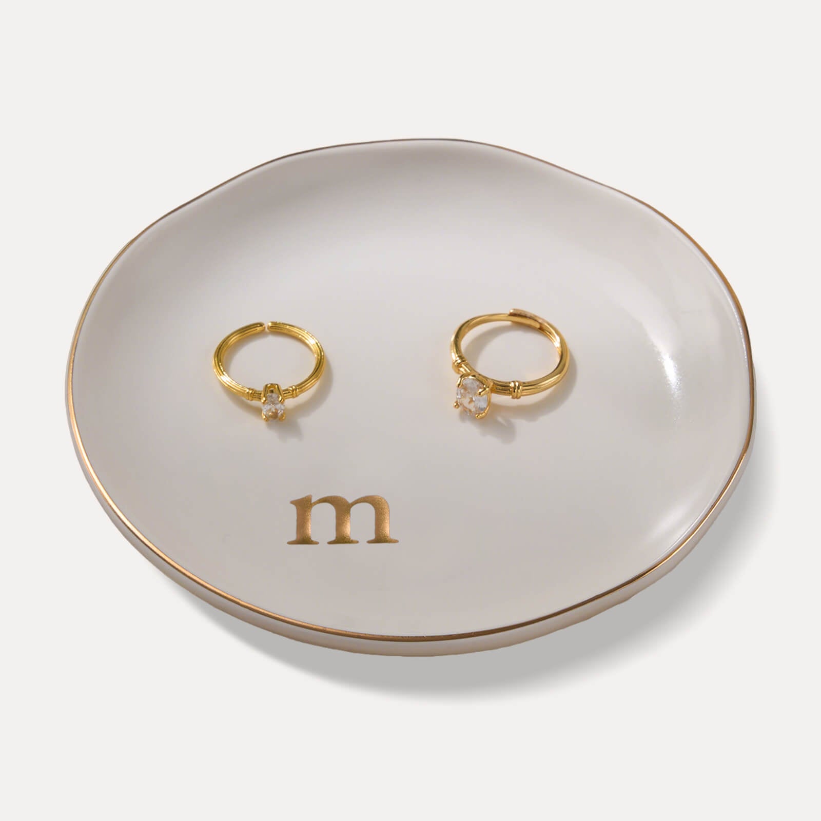 A Lolalet white ceramic jewelry dish featuring a gold "m" initial, elegantly holding an engagement ring, serving as a monogrammed ring holder.