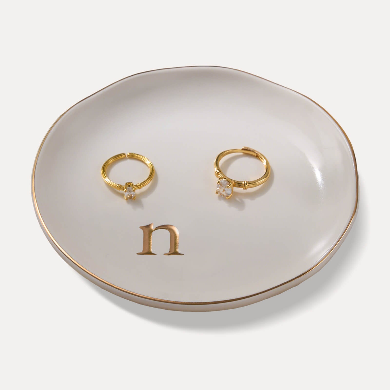 A Lolalet white ceramic jewelry dish featuring a gold "n" initial, elegantly holding an engagement ring, serving as a monogrammed ring holder.