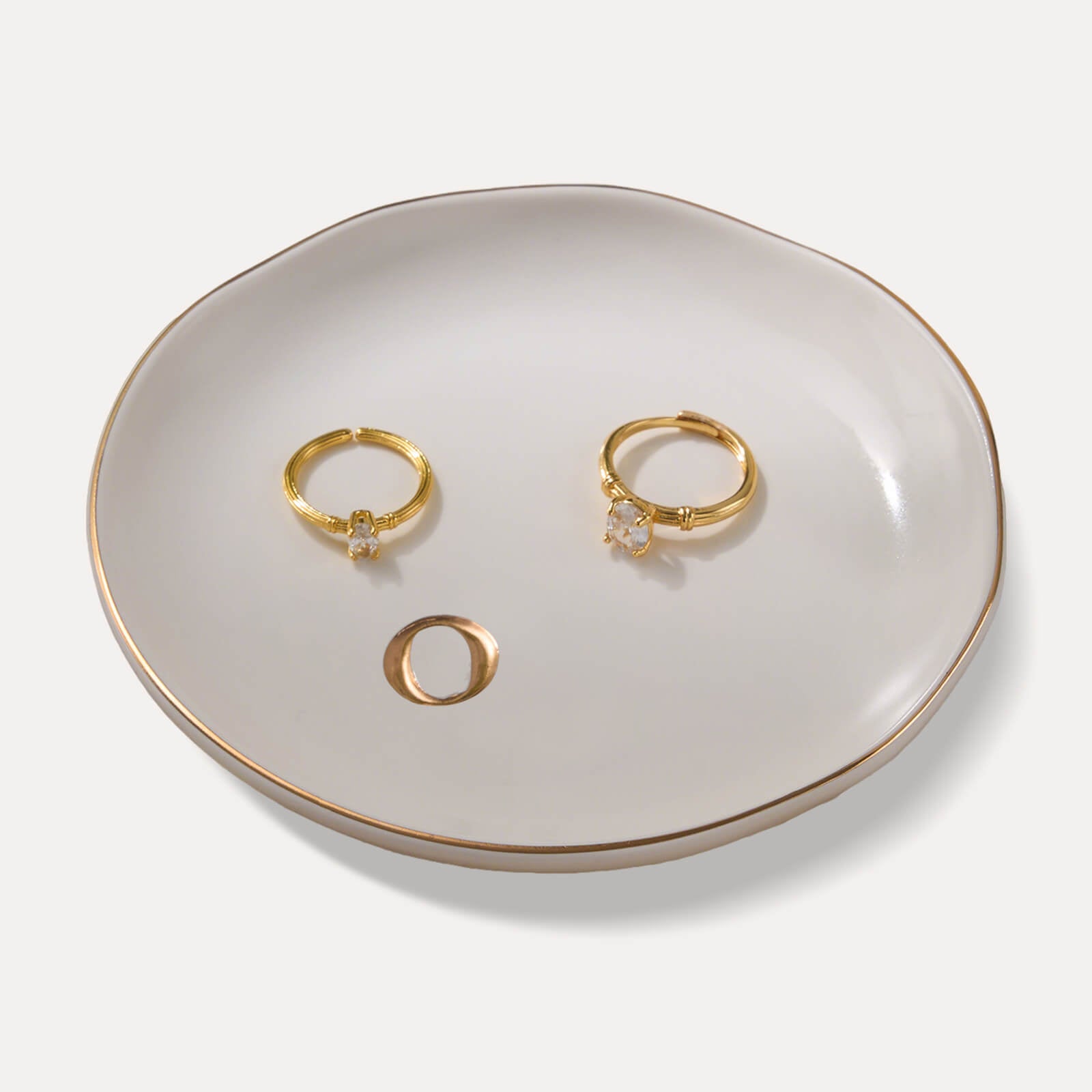 A Lolalet white ceramic jewelry dish featuring a gold "o" initial, elegantly holding an engagement ring, serving as a monogrammed ring holder.