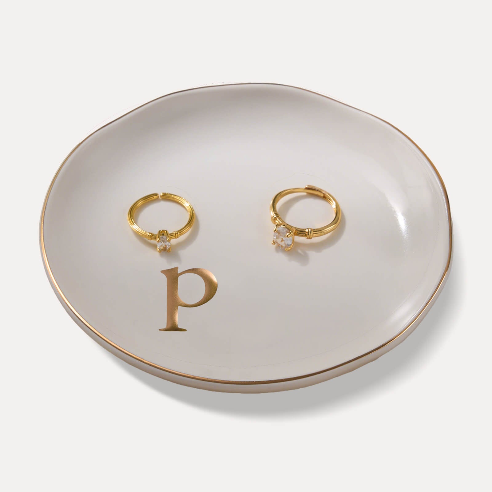 A Lolalet white ceramic jewelry dish featuring a gold "p" initial, elegantly holding an engagement ring, serving as a monogrammed ring holder.