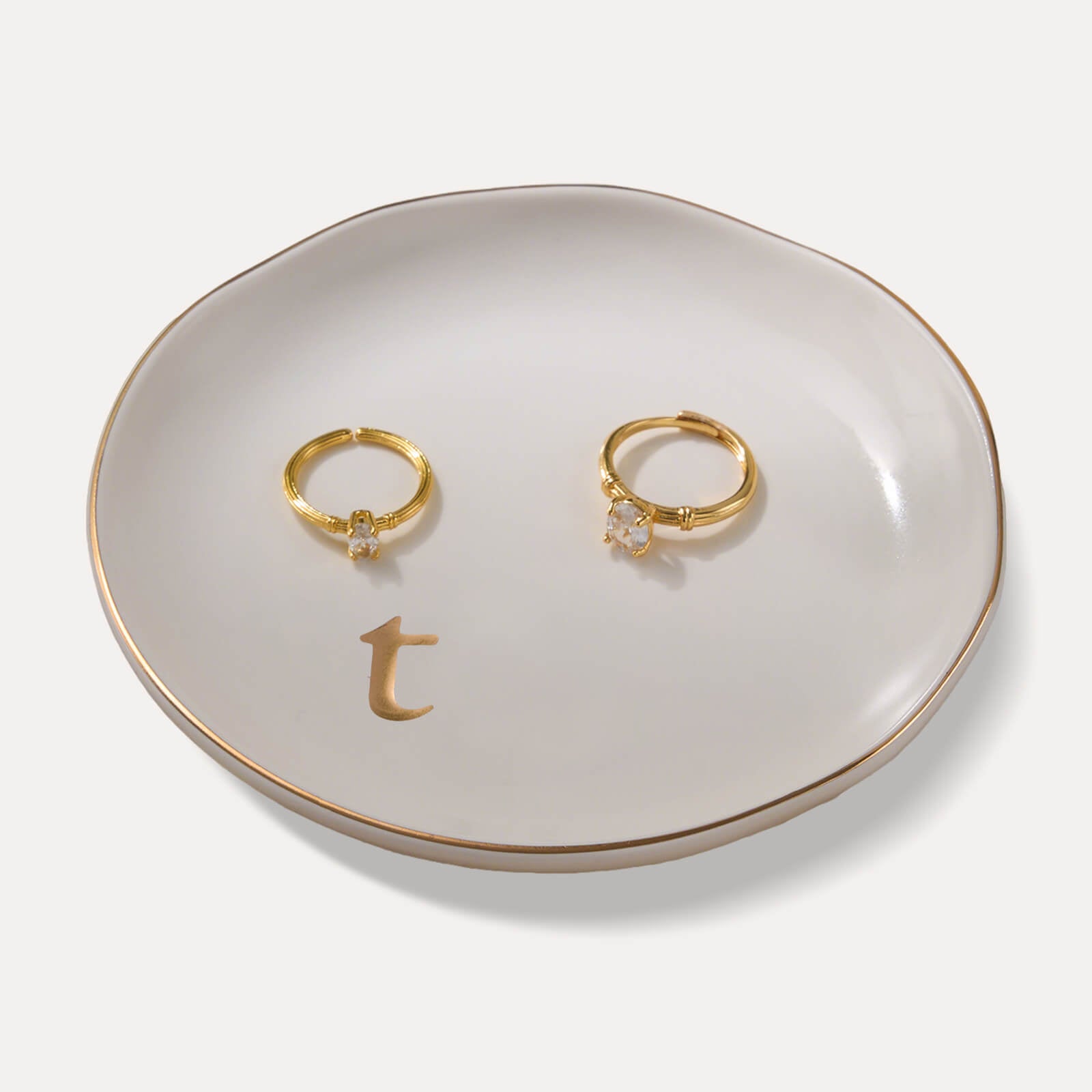 A Lolalet white ceramic jewelry dish featuring a gold "t" initial, elegantly holding an engagement ring, serving as a monogrammed ring holder.