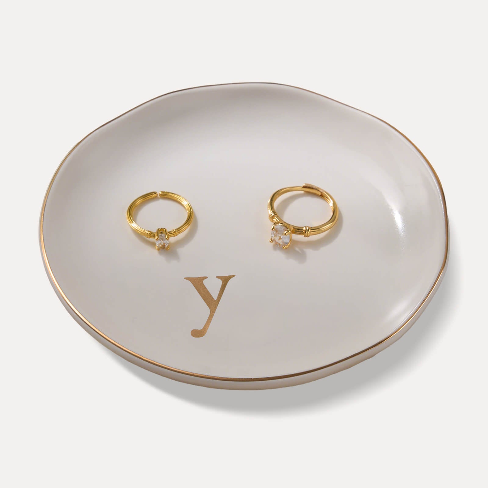 A Lolalet white ceramic jewelry dish featuring a gold "y" initial, elegantly holding an engagement ring, serving as a monogrammed ring holder.