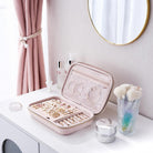 Pink jewelry case on a vanity table with various jewelry items and a mirror in the background.