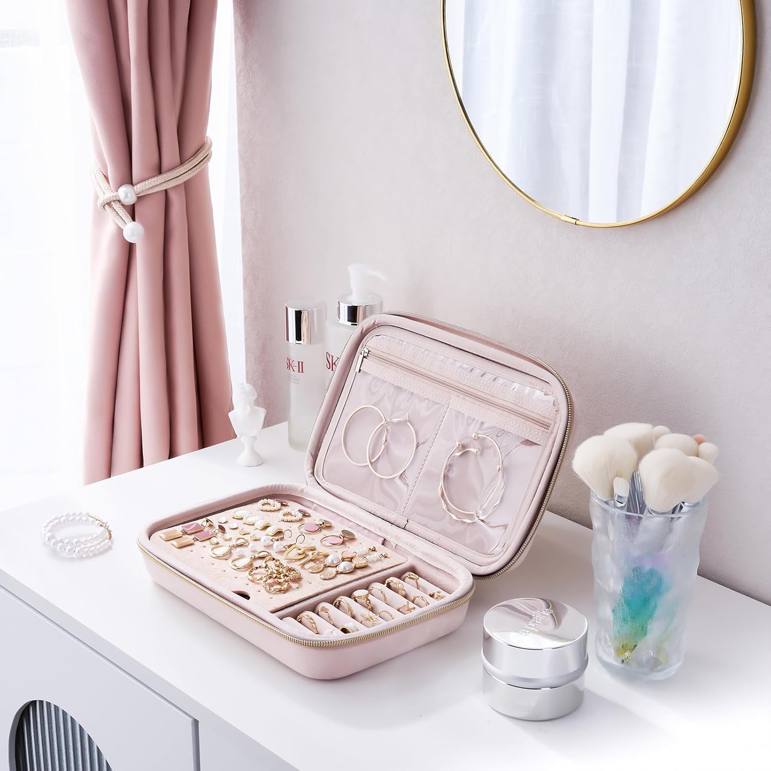 Pink jewelry case on a vanity table with various jewelry items and a mirror in the background.