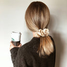 A woman with thick, long hair wearing a large pink Lolalet satin scrunchy to secure a high, voluminous ponytail