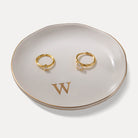 A Lolalet white ceramic jewelry dish featuring a gold "w" initial, elegantly holding an engagement ring, serving as a monogrammed ring holder.