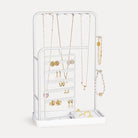 A White rotating jewelry organizer tower displaying a full collection of earrings, necklaces, bracelets, and rings.